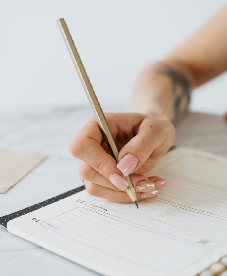 Close-up of a woman's hand writing in a notepad with a pencil.